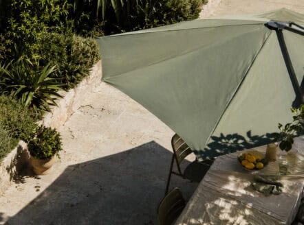 Outdoor patio with large green umbrella and dining table in garden setting.